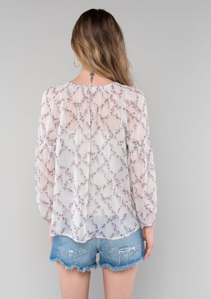 [Color: Ivory/Plum] A back facing image of a blonde model wearing a sheer chiffon spring bohemian blouse in an ivory and plum purple floral print. With long bishop sleeves, a wide smocked elastic neckline, a front keyhole detail with button closure, and a flowy relaxed fit. 