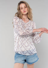 [Color: Ivory/Plum] A front facing image of a blonde model wearing a sheer chiffon spring bohemian blouse in an ivory and plum purple floral print. With long bishop sleeves, a wide smocked elastic neckline, a front keyhole detail with button closure, and a flowy relaxed fit. 