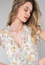 [Color: Natural/Pink] A close up front facing image of a blonde model wearing a lightweight bohemian spring peplum top in a pink floral print. With short ruffled sleeves, a ruffle trimmed v neckline, a self covered button front, and an adjustable drawstring waist with a tie. 