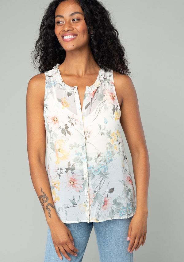 [Color: Natural/Dusty Sage] A front facing image of a brunette model wearing a sleeveless chiffon tank top in a natural and sage green floral print. With a ruffle trimmed neckline, a button front, and a split neckline. 