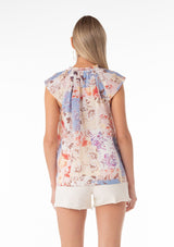 [Color: Natural/Rust] A back facing image of a blonde model wearing a lightweight cotton spring top in a pink and blue floral print. With short raglan sleeves, a ruffled neckline, lace trim, and a v neckline with double tie detail. 