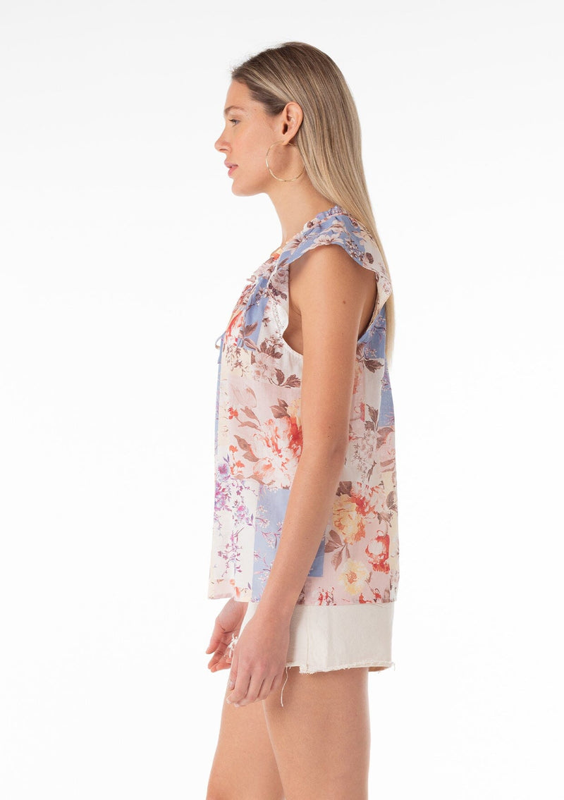 [Color: Natural/Rust] A side facing image of a blonde model wearing a lightweight cotton spring top in a pink and blue floral print. With short raglan sleeves, a ruffled neckline, lace trim, and a v neckline with double tie detail. 