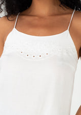 [Color: Off White] A close up front facing image of a brunette model wearing a bohemian spring camisole tank top with embroidered detail, adjustable spaghetti straps, a scooped neckline, and a self covered button up back detail. 
