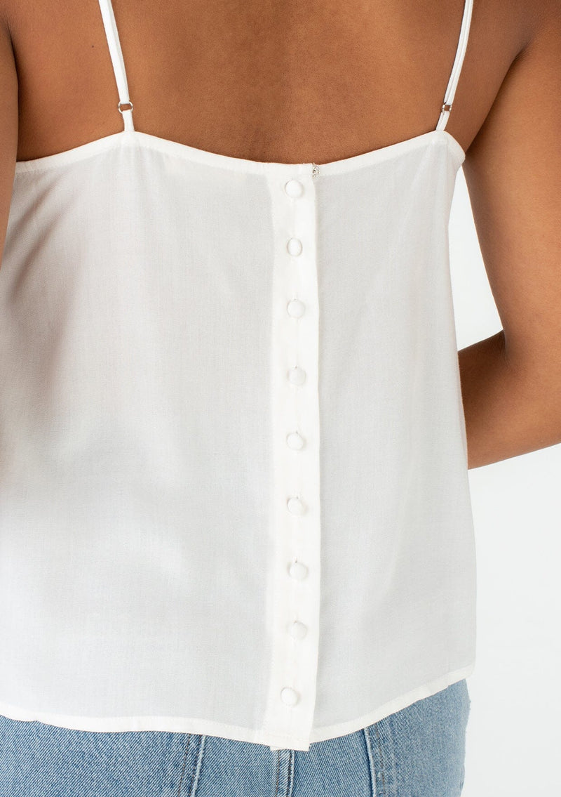[Color: Off White] A close up back facing image of a brunette model wearing a bohemian spring camisole tank top with embroidered detail, adjustable spaghetti straps, a scooped neckline, and a self covered button up back detail.  This vintage inspired white tank top features a beautiful button up back detail that will elevate any outfit you pair it with.