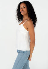 [Color: Off White] A side facing image of a brunette model wearing a bohemian spring camisole tank top with embroidered detail, adjustable spaghetti straps, a scooped neckline, and a self covered button up back detail. 
