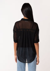[Color: Black] A back facing image of a brunette model wearing a black sheer chiffon short sleeve button front blouse. With a self covered button front and a collared neckline.