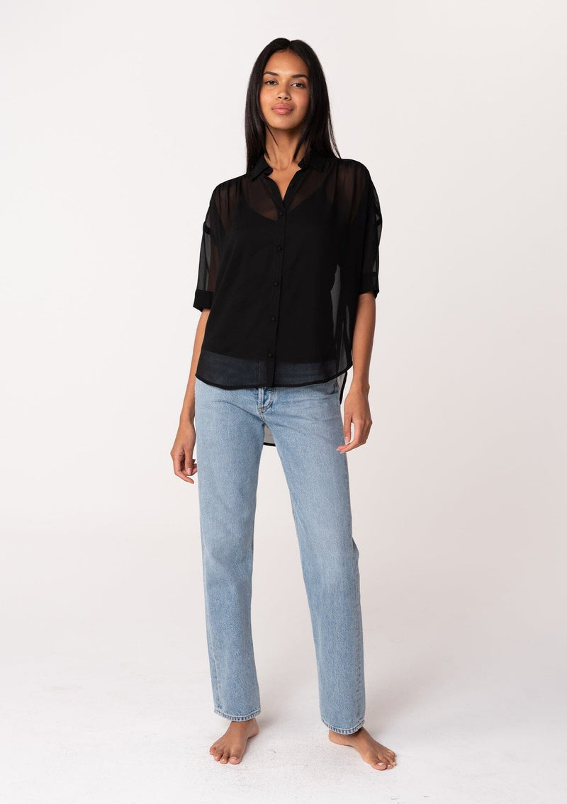 [Color: Black] A full body front facing image of a brunette model wearing a black sheer chiffon short sleeve button front blouse. With a self covered button front and a collared neckline.