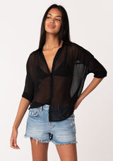 [Color: Black] A front facing image of a brunette model wearing a black sheer chiffon short sleeve button front blouse. With a self covered button front and a collared neckline.