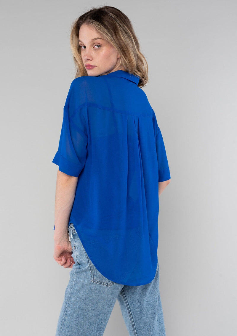 [Color: Cobalt] A back facing image of a blonde model wearing a bright blue sheer chiffon short sleeve button front blouse. With a self covered button front and a collared neckline.