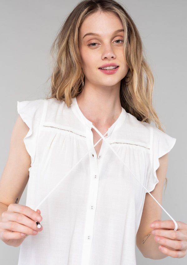 [Color: Vanilla] A close up front facing image of a blonde model wearing a solid white bohemian spring top. With short flutter cap sleeves, a self covered button front, neckline ties, and a relaxed fit. 