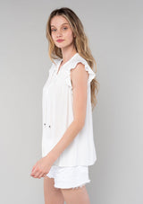 [Color: Vanilla] A side facing image of a blonde model wearing a solid white bohemian spring top. With short flutter cap sleeves, a self covered button front, neckline ties, and a relaxed fit. 