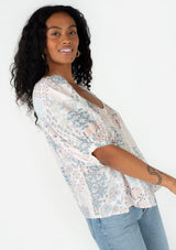 [Color: Dusty Blue/Teal] A half body side facing image of a brunette model wearing a bohemian spring blouse in a blue floral print. With half length puff sleeves, a button front, a round neckline, and a flowy relaxed fit. 