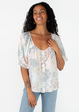 [Color: Dusty Blue/Teal] A front facing image of a brunette model wearing a bohemian spring blouse in a blue floral print. With half length puff sleeves, a button front, a round neckline, and a flowy relaxed fit. 
