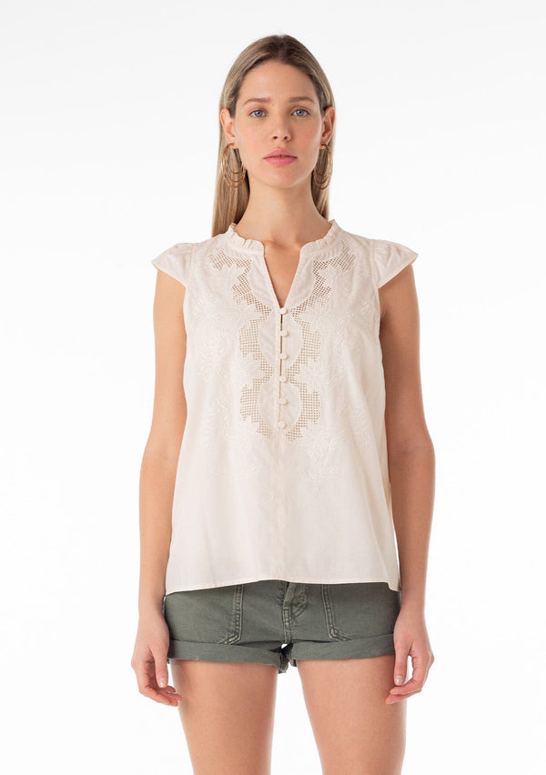 [Color: Natural] A front facing image of a blonde model wearing a bohemian cotton spring top in a natural colorway. With short cap sleeves, a self covered button front, a ruffled neckline, a v neckline, and embroidered detail. 