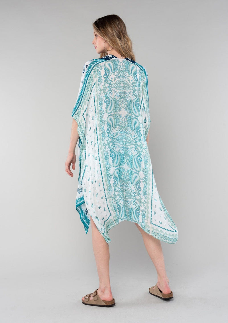 [Color: Ivory/Teal] A back facing image of a blonde model wearing a mid length bohemian kimono in an ivory and teal paisley and floral print. With half length kimono sleeves, an open front, and side slits. 