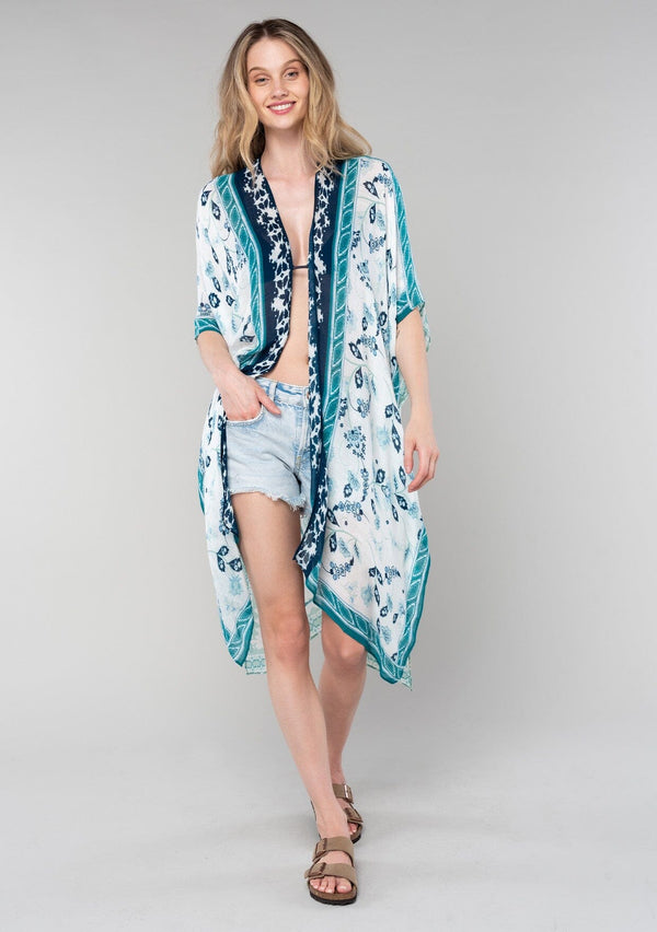 [Color: Ivory/Teal] A front facing image of a blonde model wearing a mid length bohemian kimono in an ivory and teal paisley and floral print. With half length kimono sleeves, an open front, and side slits. 