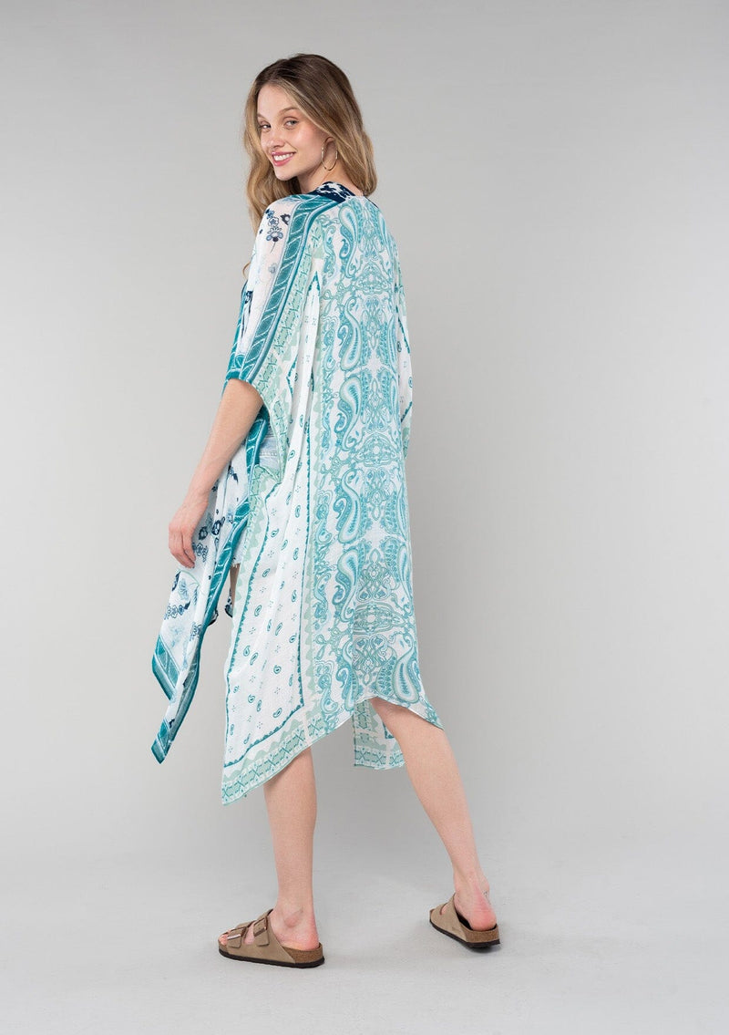 [Color: Ivory/Teal] A full body back facing image of a blonde model wearing a mid length bohemian kimono in an ivory and teal paisley and floral print. With half length kimono sleeves, an open front, and side slits. 