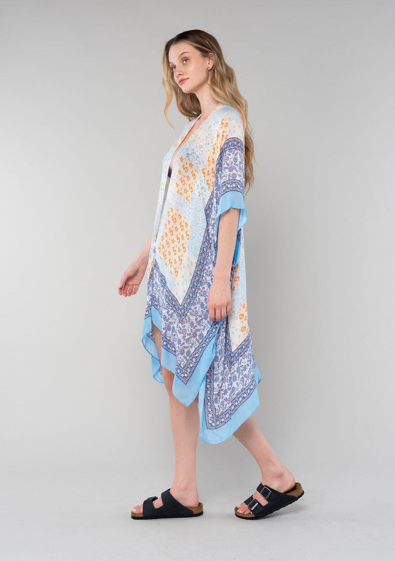 [Color: Ivory/Light Blue] A side facing image of a blonde model wearing a lightweight bohemian mid length kimono in an ivory and light blue mixed floral border print. With half length kimono sleeves, an open front, and side slits. 