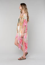 [Color: Mustard/Fuchsia] A side facing image of a blonde model wearing a lightweight bohemian mid length kimono in a mustard yellow and fuchsia pink watercolor floral print. With half length kimono sleeves, an open front, and side slits. 