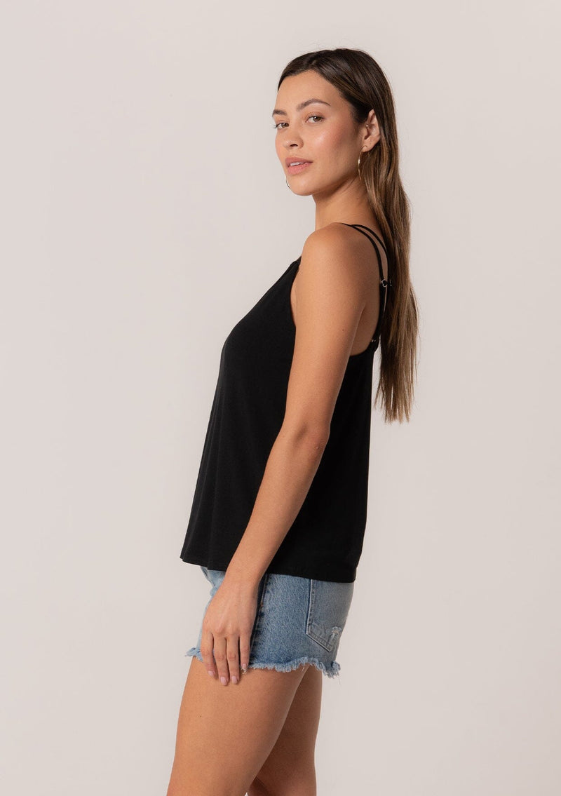 [Color: Black] A side facing image of a brunette model wearing a black stretchy bamboo knit tank top with asymmetric spaghetti straps, a scoop neckline, and a relaxed slim fit.