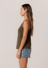 [Color: Military] A side facing image of a brunette model wearing a military green stretchy bamboo knit tank top with asymmetric spaghetti straps, a scoop neckline, and a relaxed slim fit.