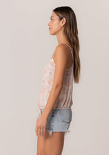 [Color: Natural/Peach] A side facing image of a brunette model wearing a summer tank top in a pink bohemian print. With adjustable spaghetti straps, a scoop neckline, a button front, a drawstring waist with tassel ties, and a relaxed fit. 