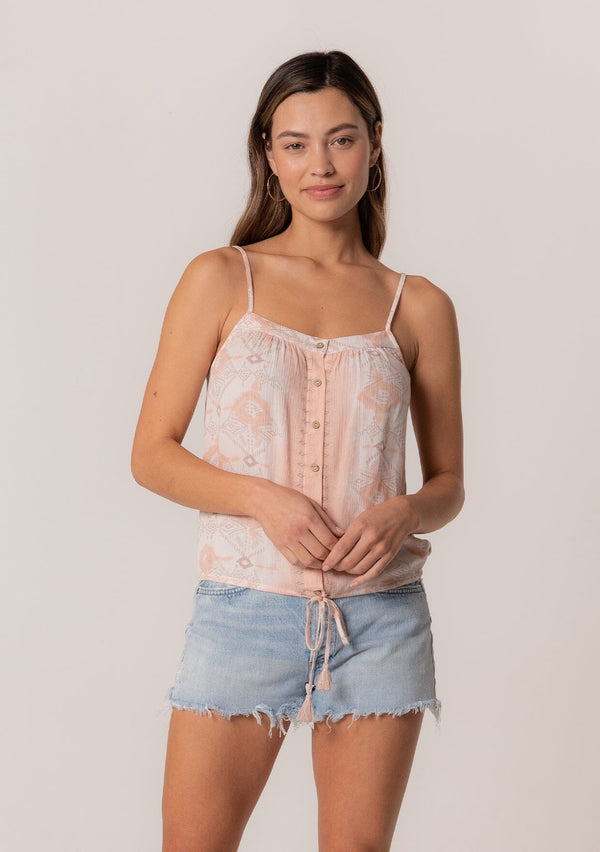 [Color: Natural/Peach] A front facing image of a brunette model wearing a summer tank top in a pink bohemian print. With adjustable spaghetti straps, a scoop neckline, a button front, a drawstring waist with tassel ties, and a relaxed fit. 