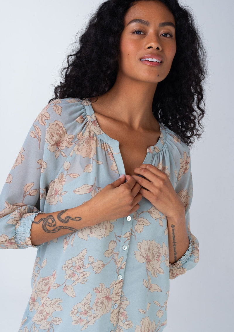 [Color: Dusty Blue/Natural] A close up front facing image of a brunette model wearing a bohemian spring sheer chiffon blouse in a dusty blue and natural floral print. With three quarter length sleeves, a button front, and a split v neckline. 