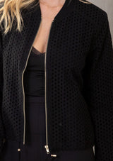 [Color: Black] A model wearing an allover eyelet black zip up bomber jacket.