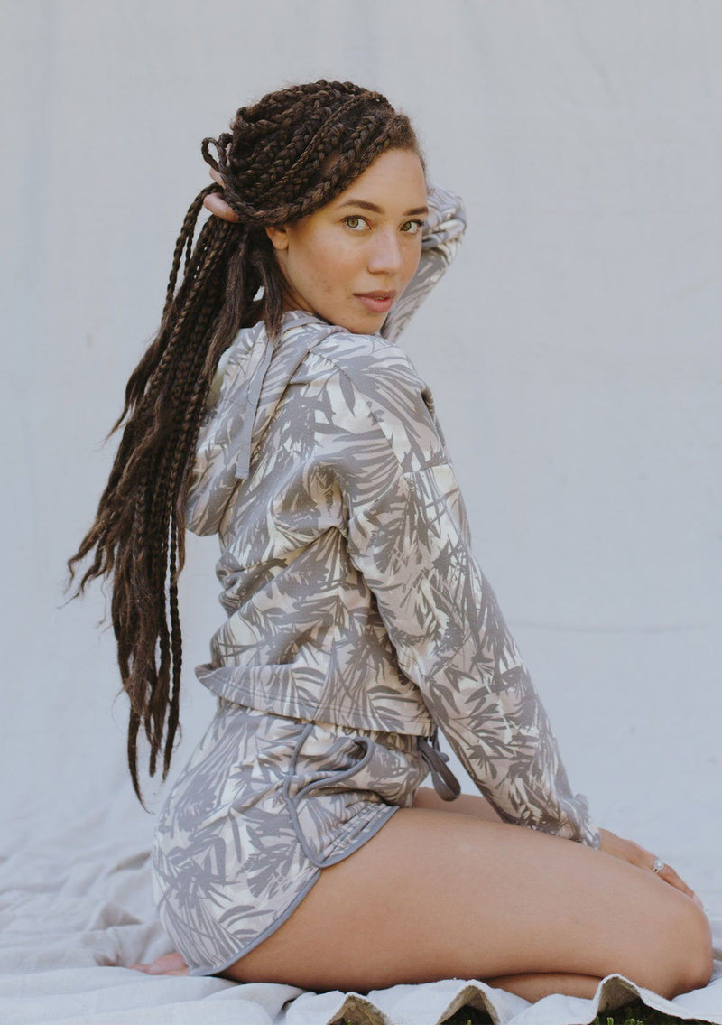 [Color: Grey/Natural] A woman standing outside against a white backdrop wearing a palm print jogging short. Featuring a drawstring waist, contrast trim, and essential side pockets.