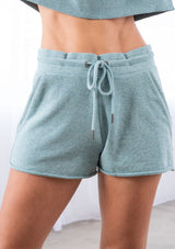 [Color: Sea Blue] A model wearing a classic sea blue lounge short. With side pockets, an elastic waist with drawstring, and a raw unfinished hem. 