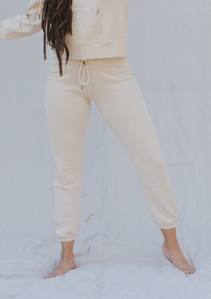 [Color: Sand] A woman outside wearing a classic jogger pant with a drawstring waistband, a slim tapered leg, and a contrast side stitch detail. 