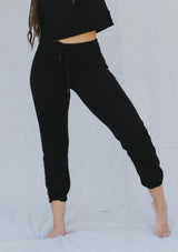 [Color: Black] A woman outside wearing a classic jogger pant with a drawstring waistband, a slim tapered leg, and a contrast side stitch detail. 