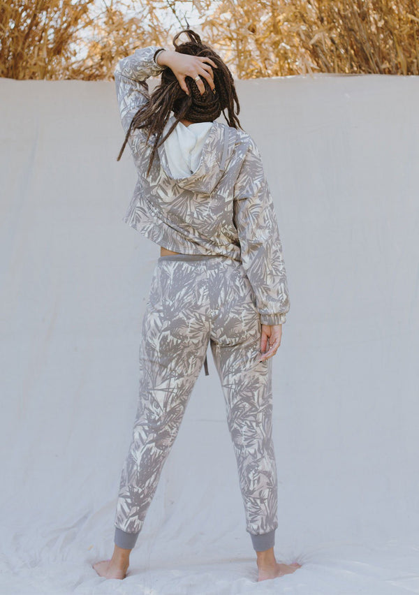 [Color: Grey/Natural] A woman standing outside wearing a palm print jogging pant. Featuring a drawstring waist, contrast trim, and essential side pockets.