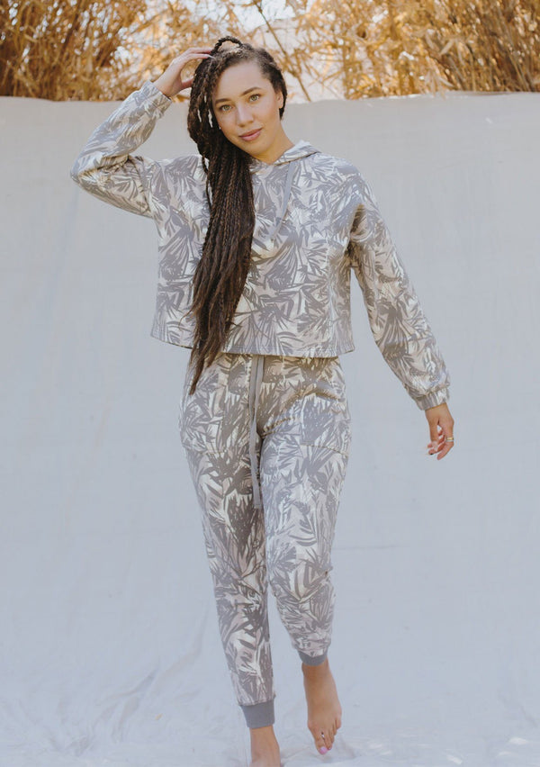 [Color: Grey/Natural] A woman standing outside wearing a palm print jogging pant. Featuring a drawstring waist, contrast trim, and essential side pockets.