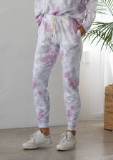 [Color: Lavender Combo] A woman standing outside wearing a classic cotton jogger pant in a splatter tie dye wash. Featuring a drawstring waistband, side pockets, and a slim leg.