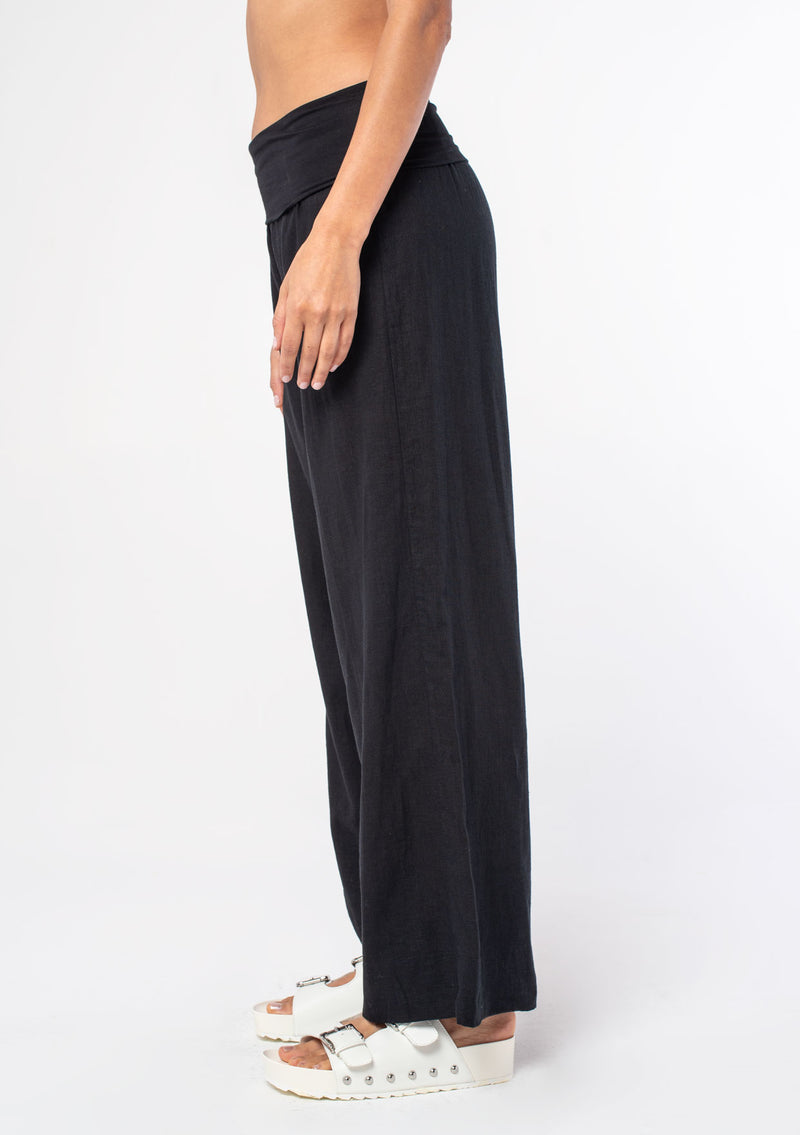 [Color: Black] A model wearing a cool black lounge pant in a cotton linen blend. With a long wide leg and a contrast knit fold over waistband.