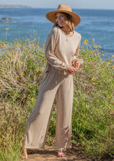 [Color: Almond] A woman standing outside on the beach wearing a cropped wide leg pant. Featuring an elastic waistband and an embroidered trim along the side.