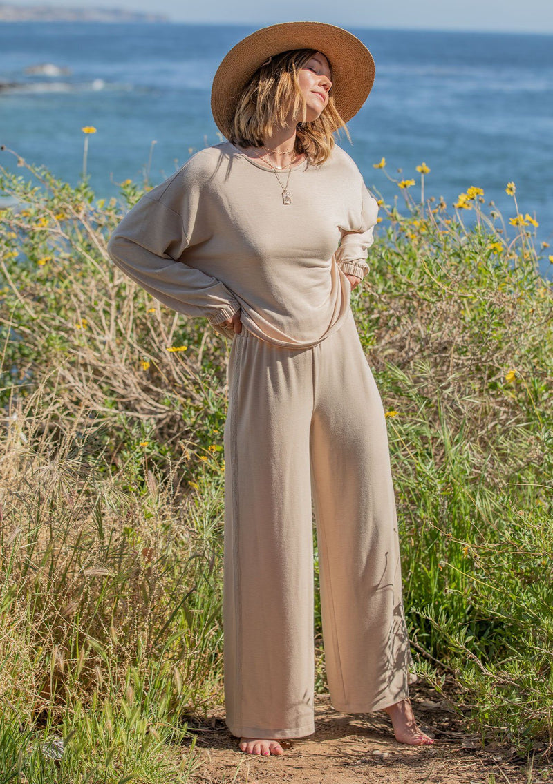 [Color: Almond] A woman standing outside on the beach wearing a cropped wide leg pant. Featuring an elastic waistband and an embroidered trim along the side.