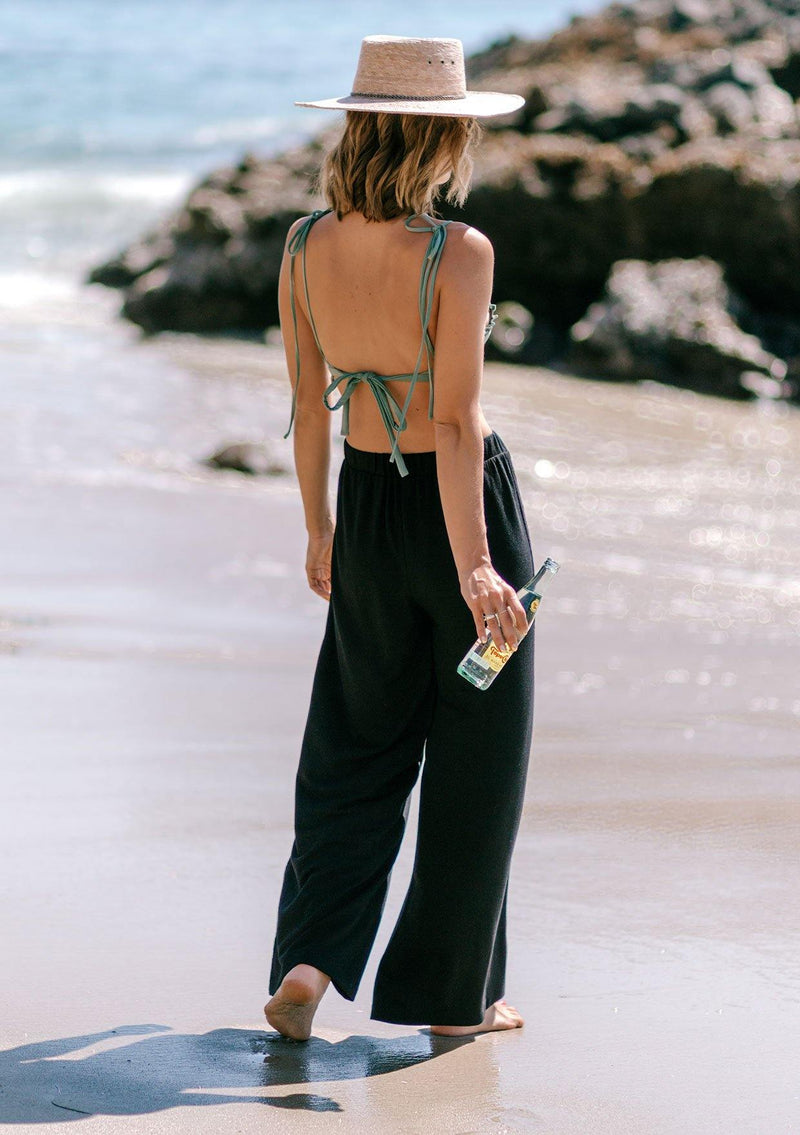 [Color: Black] A woman standing outside on the beach wearing a cropped wide leg pant. Featuring an elastic waistband and an embroidered trim along the side.