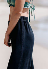 [Color: Black] A woman standing outside on the beach wearing a cropped wide leg pant. Featuring an elastic waistband and an embroidered trim along the side.