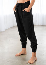 [Color: Black] A model wearing a woven jogger pant. With essential cargo style side pockets, an elastic drawstring waist, and ankle length tapered leg.