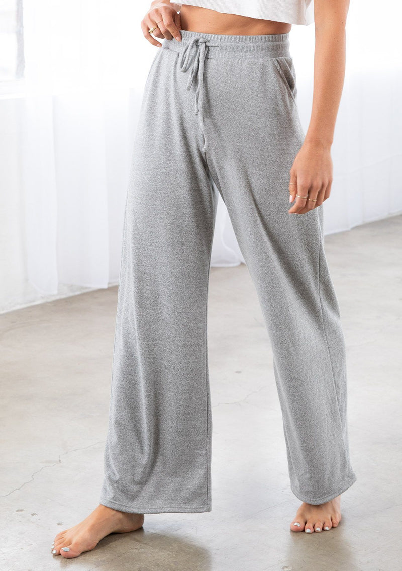[Color: Light Heather Grey] A model wearing a soft knit wide palazzo leg pant. Featuring an elastic drawstring waistband and side pockets.