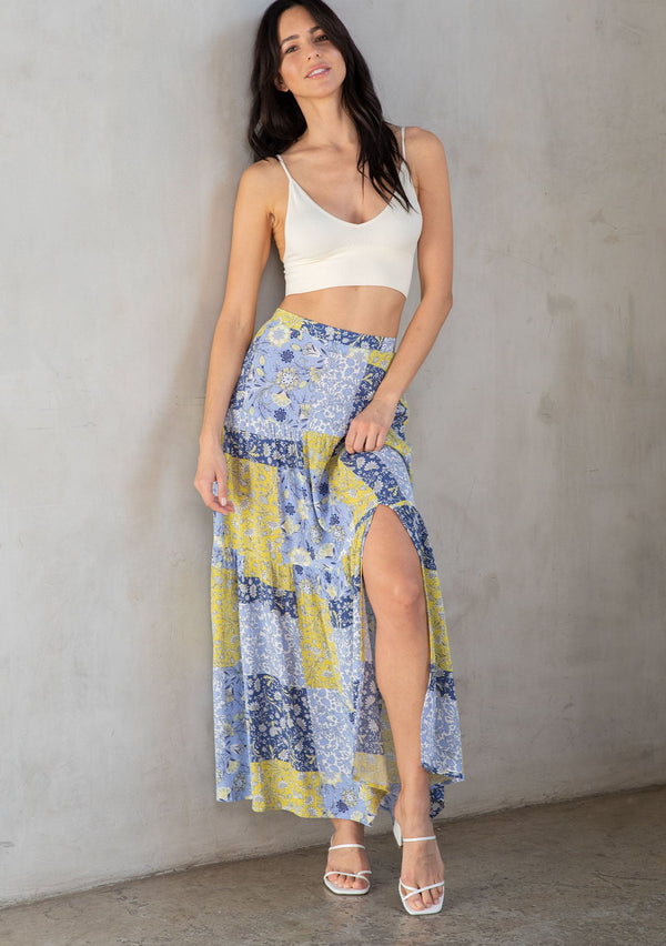 [Color: Blue/Lime] A model wearing a blue and lime green patchwork floral print maxi skirt with a side slit. 