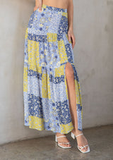 [Color: Blue/Lime] A model wearing a blue and lime green patchwork floral print maxi skirt with a side slit. 