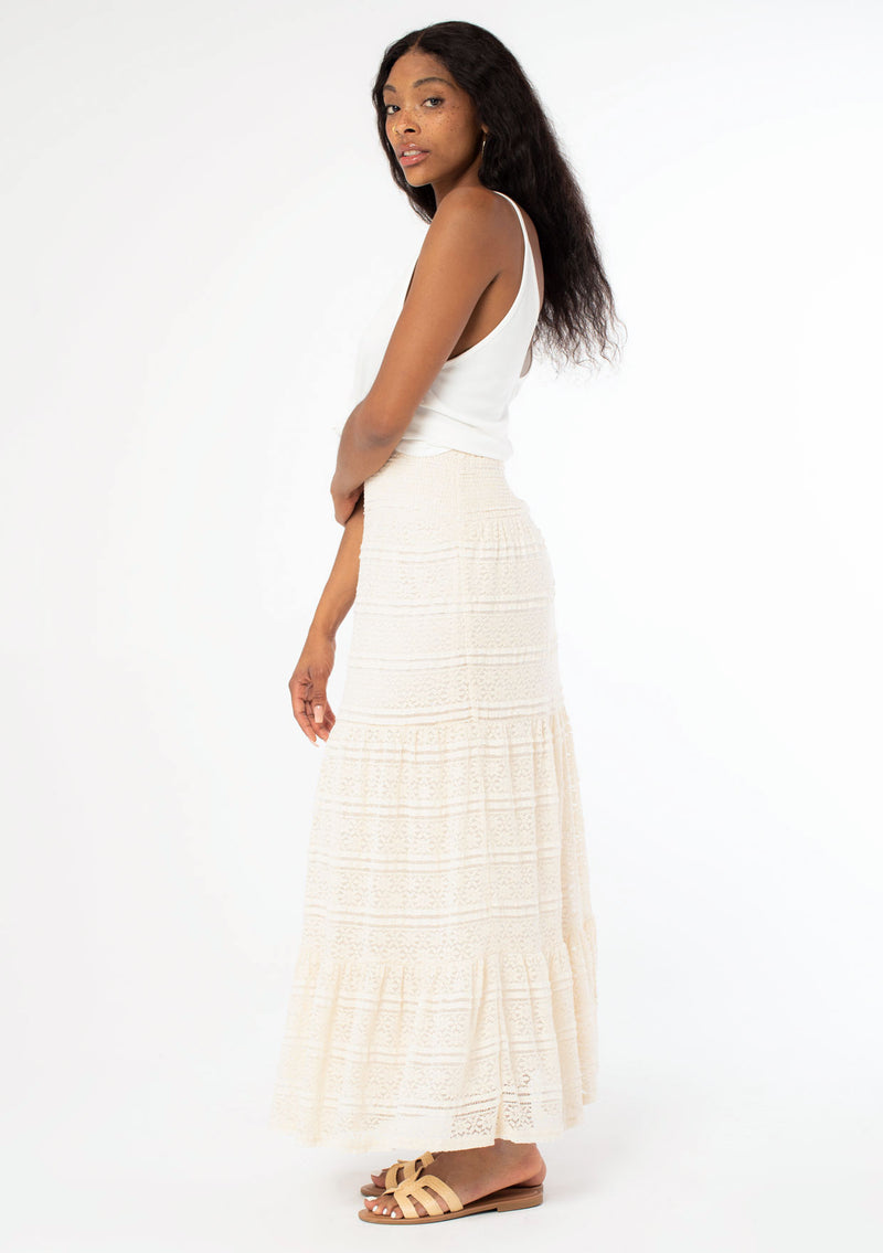 [Color: Natural] A side facing image of a black model wearing a bohemian off white lace maxi skirt.