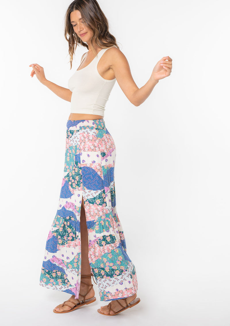 [Color: Ivory/Jade] A model wearing a blue and pink floral patchwork print maxi skirt with a side slit. 