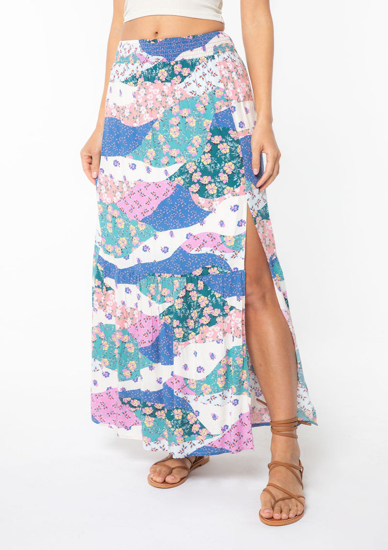 [Color: Ivory/Jade] A model wearing a blue and pink floral patchwork print maxi skirt with a side slit. 