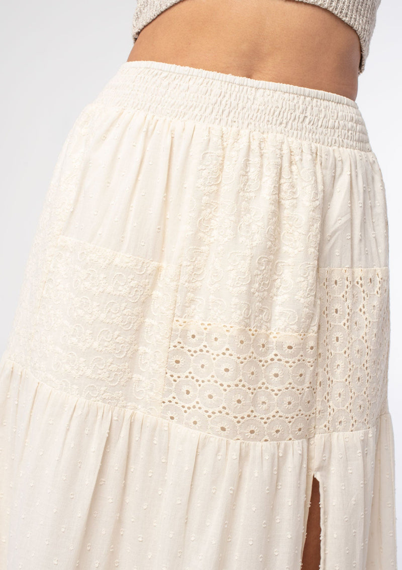 [Color: Natural] A woman wearing a bohemian off white cotton maxi skirt with embroidered detail throughout. 