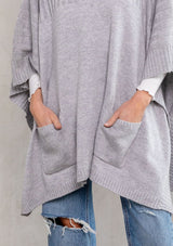 [Color: Light Heather Grey] A model wearing a cozy heather grey turtleneck sweater poncho. 